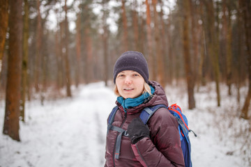 Photo of side view of smiling girl in hat with backpack over winter forest