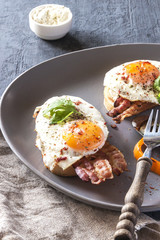 Sandwich, toast with bacon, sauce and poached egg on grey plate on dark background vertically.