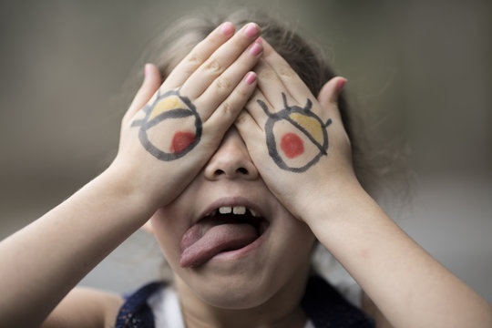 Little girl with cartoon eyes painted on her hands making silly face.