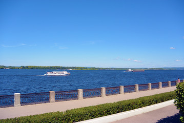 Obraz premium View on the Volga quay of the Samara city in sunny summer day. City embankment, barge and touristic motor ship boat on river, clear blue sky