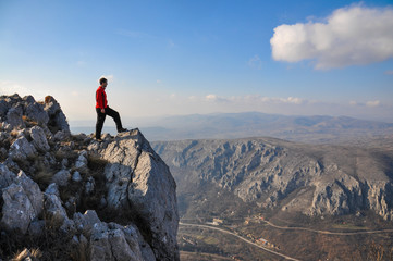 Young man on a cliff edge on the top of mountain with gorgeous view. Hiker on mountain peak on...