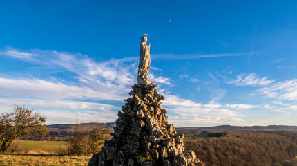 Wide angle shot from low angle of view of a Virgin Mary statue with moon and clouds on background. - 192182362