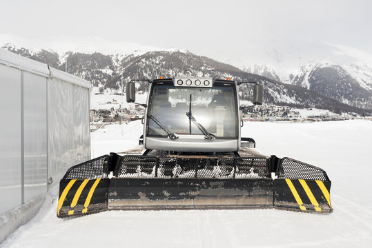 A front view of a snowcat and a town at the background in the alsp switzerland