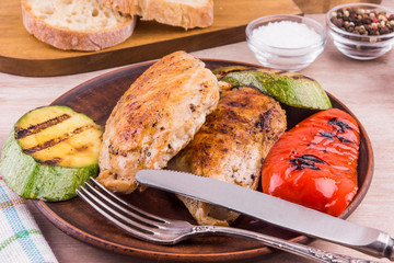 Fried chicken fillet with grilled vegetables in a plate on a rustic wooden table - close-up