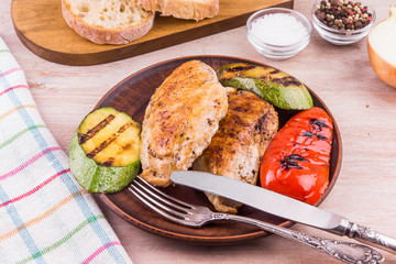 Fried chicken fillet with grilled vegetables in a plate on a rustic wooden table