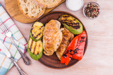 Fried chicken fillet with grilled vegetables in a plate on a rustic wooden table - top view