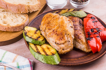 Fried chicken fillet with grilled vegetables in a plate on a rustic wooden table - close-up