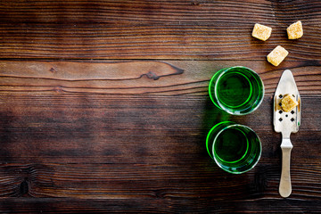 Traditions of drinking absinthe. Special spoon and sugar cubes near shots on dark wooden background top view copy space