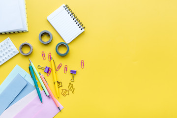 Scattered stationery on student's desk. Yellow background top view copy space