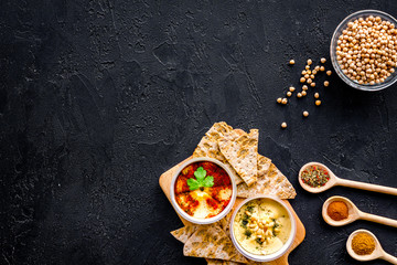 Hummus ready to eat. Bowl with dish among pieces of crispbread and spices on black background top view copy space