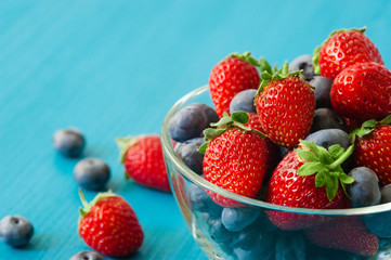 glass bowl with assortment berries blueberries, strawberries over wooden table. Natural day light. Top view
