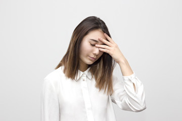 Indoor portrait of sad and disappointed young asian woman covering her face with hands in white formal shirt. Emotions, feelings, lifestyle concept.