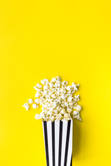 Popcorn in paper bag scattered on yellow background top view copy space