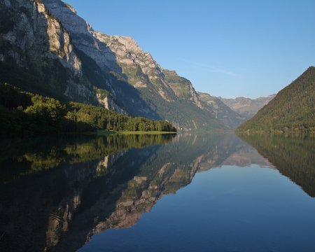 Summer morning at lake Klontalersee, Switzerland. Mountain range mirroring on the surface.