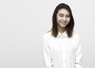 Obraz premium Indoor portrait of young attractive shy woman smiling in white formal shirt on the white background. Emotions, feelings, lifestyle concept