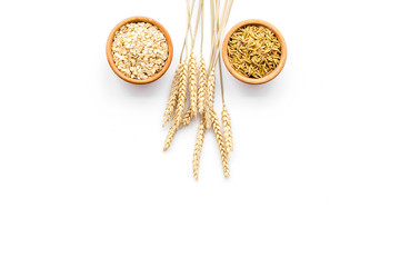 Oatmeal and oat in bowls near sprigs of wheat on white background top view copy space