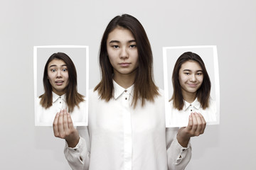 Indoor photo of woman holding two different portraits of herself with scared face and happy face. Different emotions and facial expressions concept
