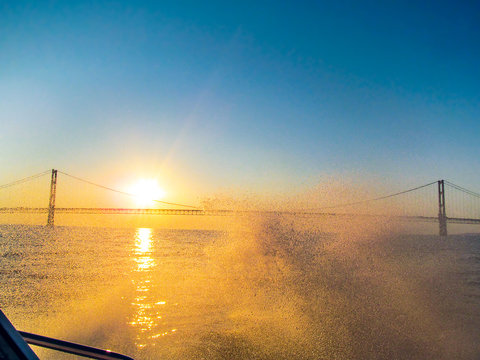 Mackinac Bridge and bright sun rays are visible through water splashes.
View from the lake surface when the boat moves at high speed and creates a waves and water sprays at sunset in Michigan, USA.