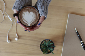 Top view female hands holding a cup of hot coffee with heart shape latte art. with copy space.