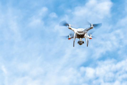 White Drone flying in a cloudy blue sky.