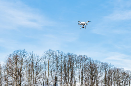 White Drone flying in a cloudy blue sky.