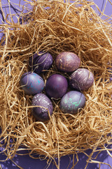 top view of traditional purple easter eggs in straw nest