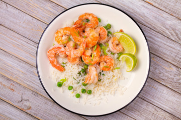 Shrimps with ginger rice and green peas, lime on white plate on wooden background
