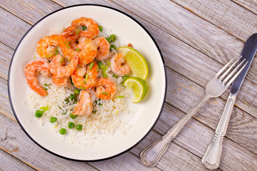 Shrimps with ginger rice and green peas, lime on white plate on wooden background