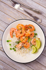 Shrimps with ginger rice and green peas, lime on white plate on wooden background