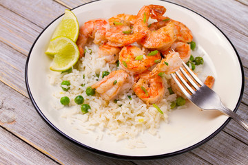 Shrimps with ginger rice and green peas, lime on white plate on wooden background