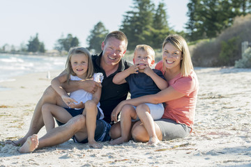Fototapeta premium happy beautiful Caucasian family having holidays on the beach smiling with mother and father sitting on sand with little son and young daughter