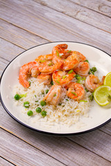 Shrimps with ginger rice and green peas, lime on white plate on wooden background