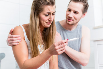 Young woman is sad about result of pregnancy test and her husband is comforting and hugging her 