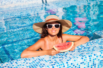 A girl holds half a red watermelon  over a blue pool, relaxing on spa in a tropical hotel, eating healthy, fruit diet, summer style