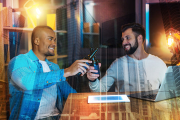Cheers. Cheerful young friends clanging bottles and smiling while drinking beer and relaxing in the evening together