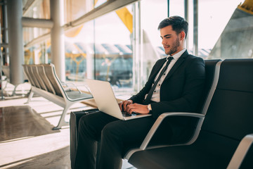 Young business man sitting on the computer with the suitcase at the airport waiting for the flight