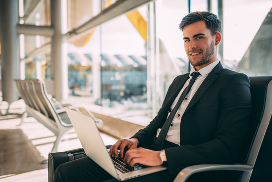 Young business man sitting on the computer with the suitcase at the airport waiting for the flight