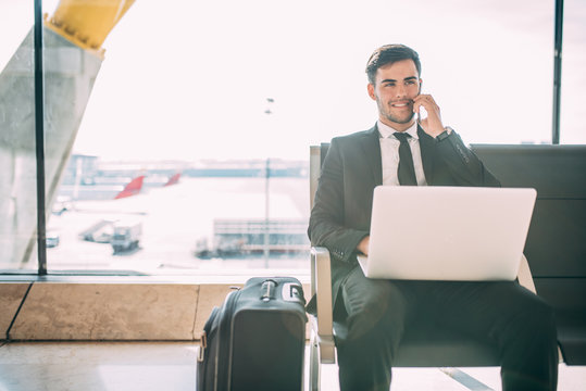 Young business man sitting on the computer and mobile phone with the suitcase at the airport waiting for the flight
