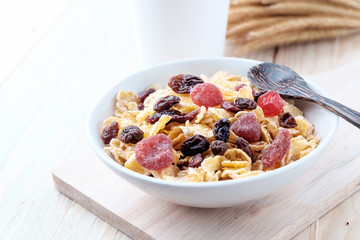 cornflakes and dry berry fruits in a white bowl on a wooden background.
