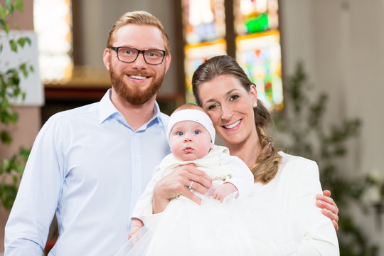Young parents at the church with their baby wearing a christening gown 