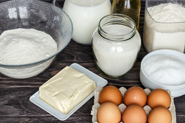Ingredients for pancakes: milk, eggs, sugar, salt, flour, vegetable oil on a wooden white background.