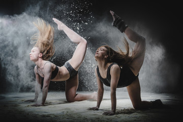 Two girls dance with flour on black background
