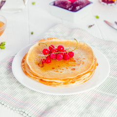 Thin pancakes with red currant berries on the served white wooden table. Rustic style. Traditional for the Russian pancake week (Maslenitsa). Selective focus, space for text. Square card.
