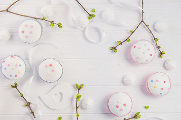 Top view Easter holiday composition of branches with young shoots of greenery, decorated cupcakes, merengue sweets, ribbon and colored bird figure on wooden background. Art concept. Selective focus.