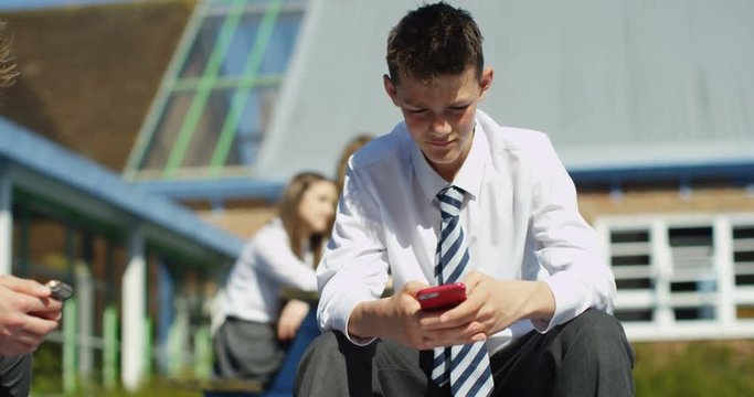 4K School kids staring intently at their smartphones outside school building - lack of social interaction. Slow motion