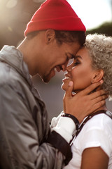 Vertical close up portrait of happy peased people in love being of different nation, express their good relationship and feelings. Dark skinned male in trendy hat looks sincerely in girlfriend s eyes.