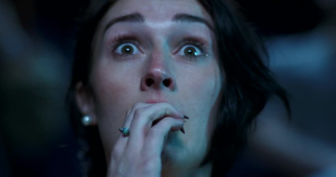 Young woman at the movie theatre reacting to a scary film