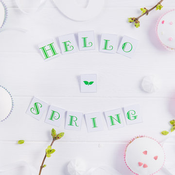 Top view composition of Hello spring lettering, branches with young shoots of greenery, easter cupcakes, merengue sweets, handcraft bird figure on wooden background. Art concept. Selective focus.