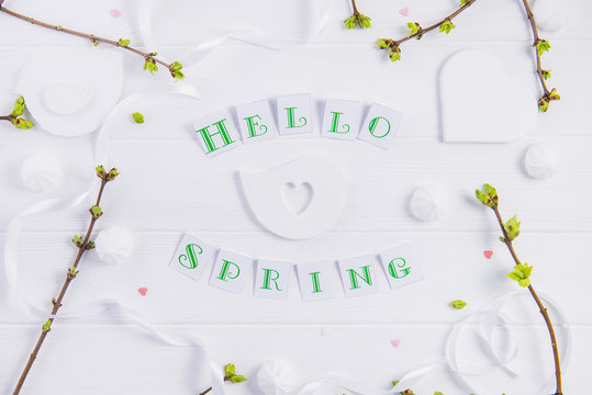 Simple composition of Hello spring calligraphy lettering and branches with young shoots of greenery on wooden background. Art concept. Selective focus. Top view. Space for text.