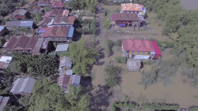 Aerial drone shot : Bird eye view of worst flooding ravaging Southeast Asia; People riding bikes on a flooded street village in rural area